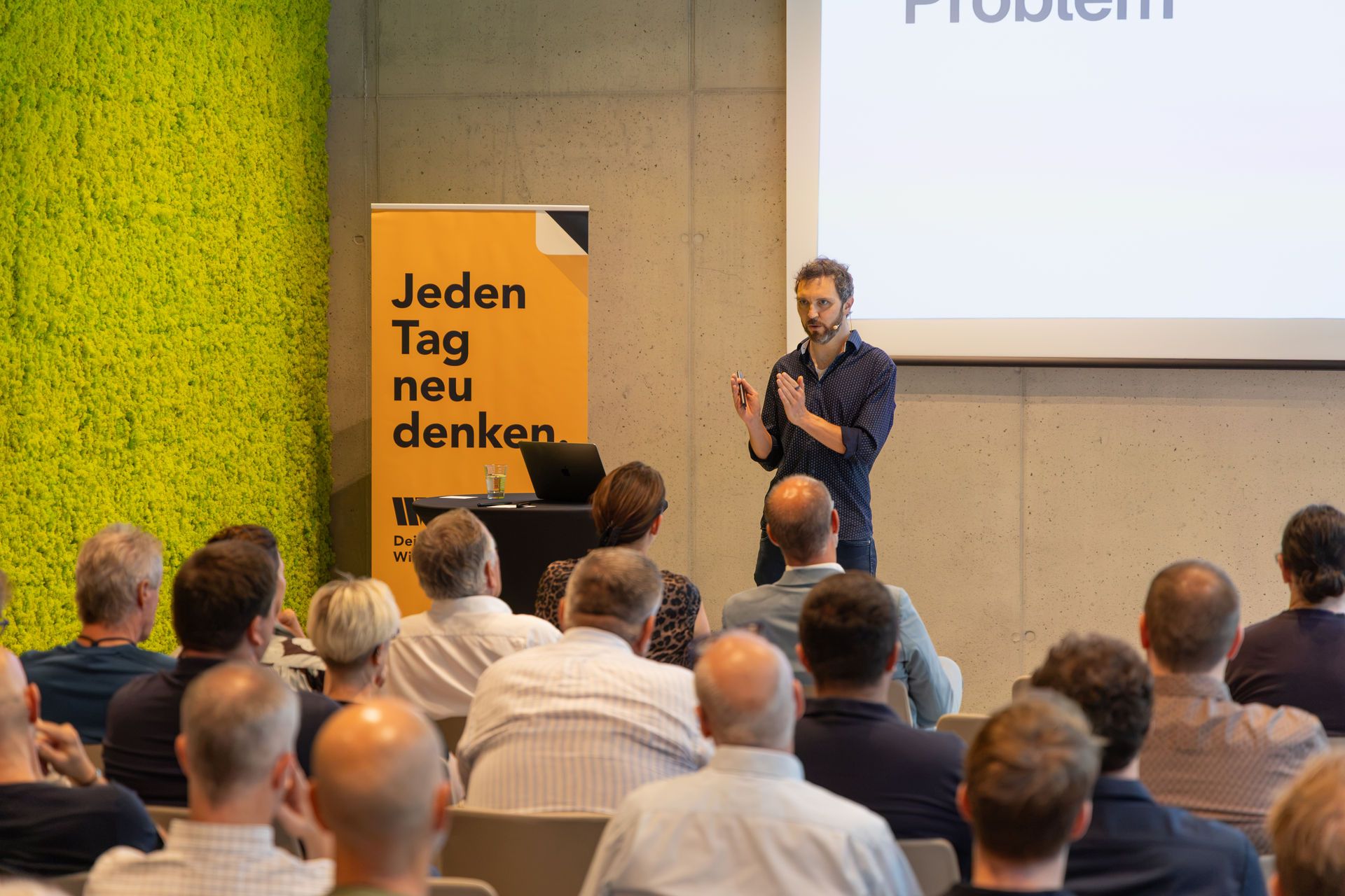 Stefan Sinnegger spricht vor sitzendem Publikum; auf der Leinwand hinter ihm steht das Wort „Problem“.
